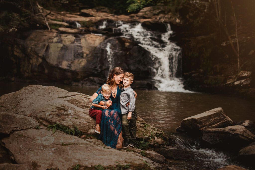 Mom sitting with her two sons on a large rock with the sliding rock and waterfall behind them.