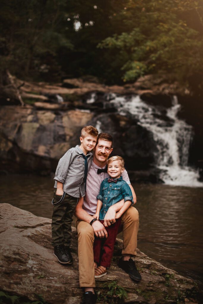 Dad kneeling with his two sons on rocks with Cochran Mill Falls waterfall in backround in Chattahoochee Hills, GA.