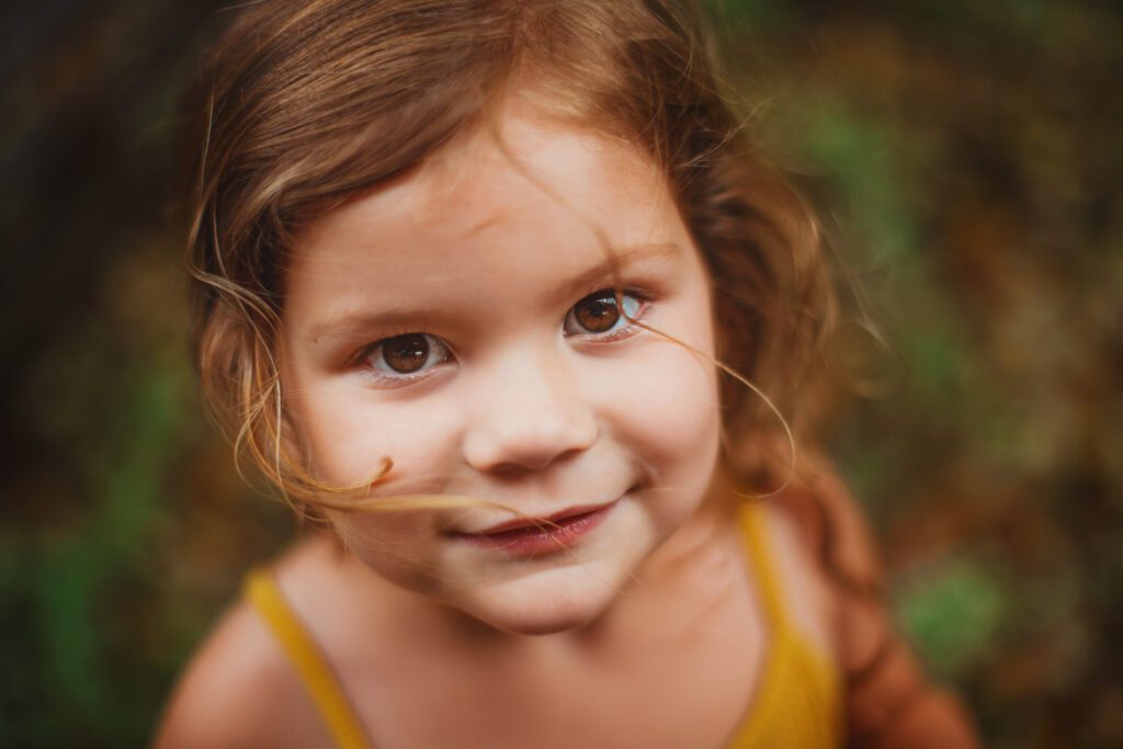 Close-up portrait of a young daughter in a mustard top looking toward the camera during family photos