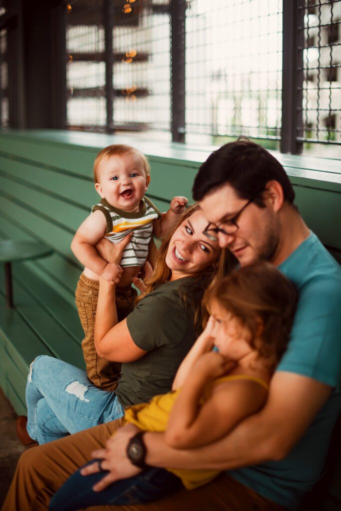 Parents and siblings laughing together beside colorful stained-glass-style windows and brickwork at Ponce City Market