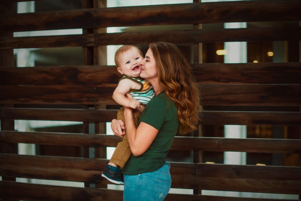 Mom holding her smiling son beside dark wooden slats along the trestle walkway connecting to the Atlanta BeltLine