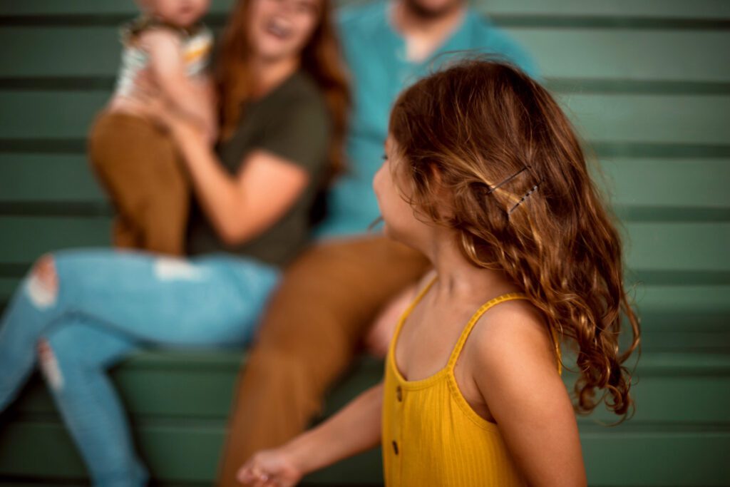 Daughter turning toward her parents during a candid family moment beside a teal bench.