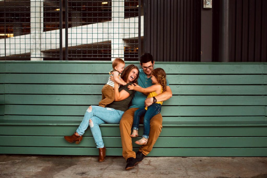 Parents sitting with their daughter and son on a teal bench beneath large original steel-framed windows