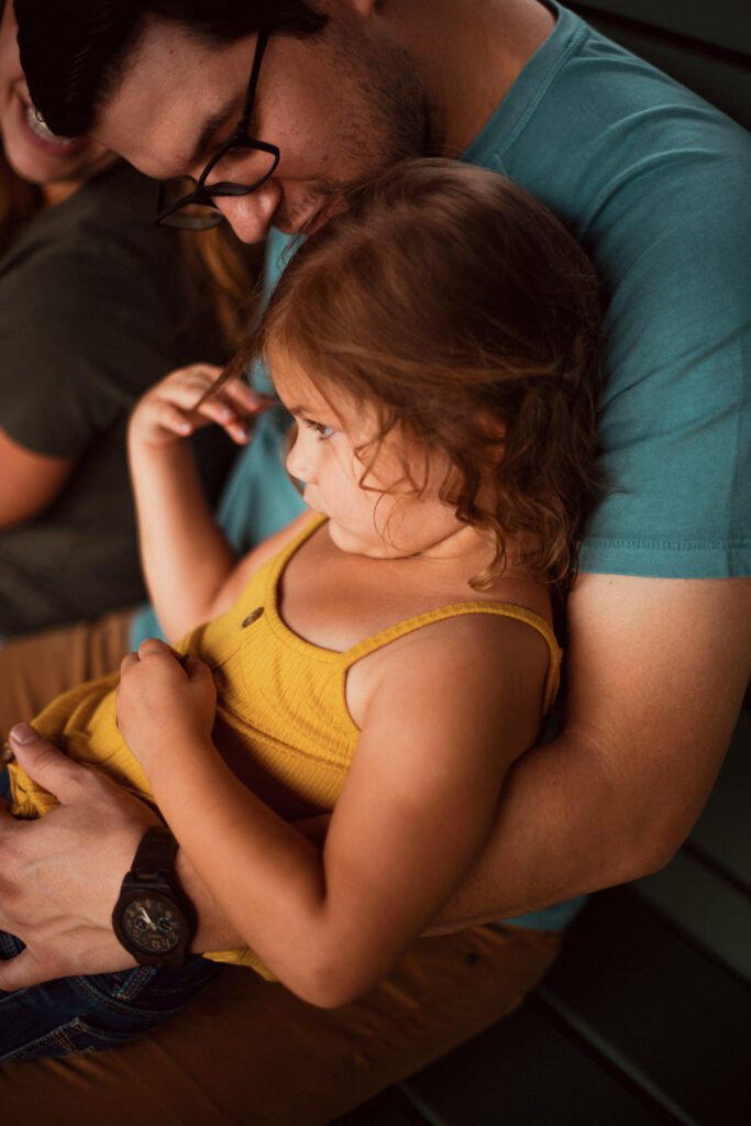 Dad holding his daughter on his lap while seated on a teal bench
