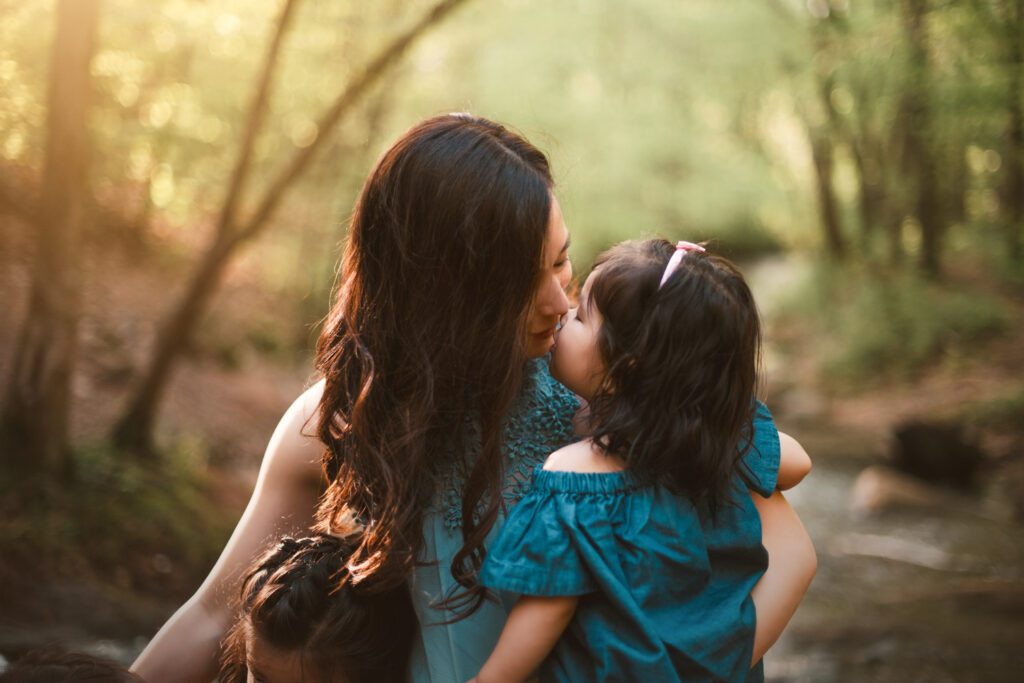 Mom kissing her young daughter while holding her beside the rocky creek at sunset