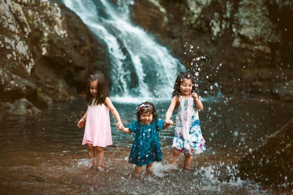 Three sisters splashing through shallow water and waterfall