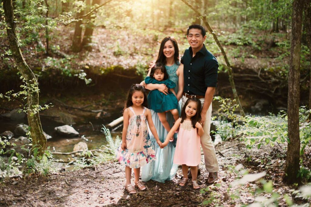 Parents standing with their three daughters beside creek in a forest setting