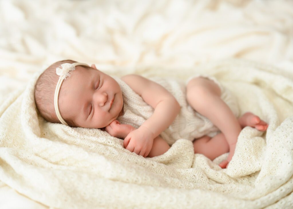 Peaceful newborn baby girl sleeping on a delicate knit blanket with one hand tucked beneath her cheek.
