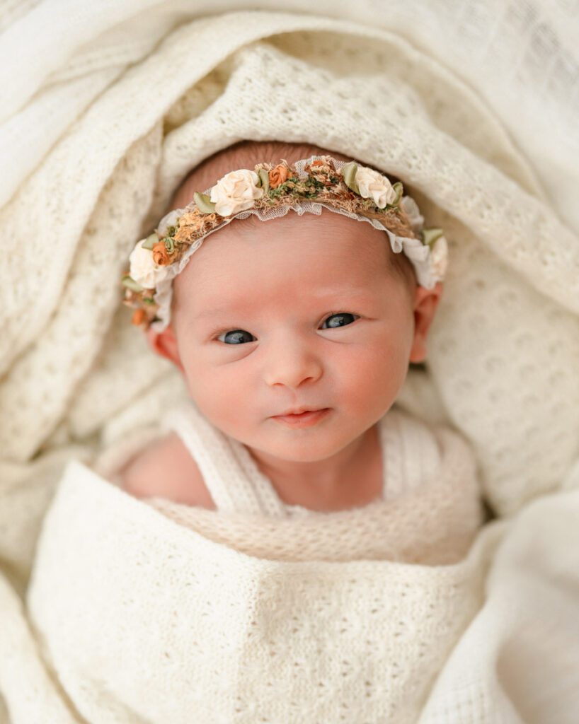 Alert newborn baby girl in a floral headband looking toward the camera during a Roswell newborn photo session.