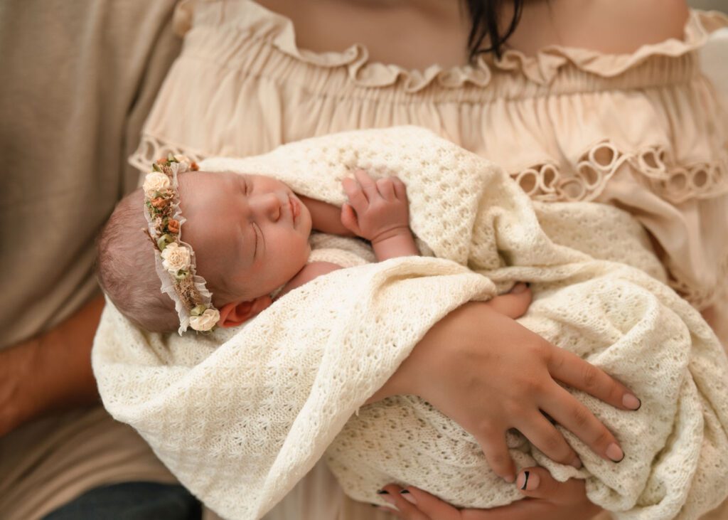 Family standing by a bright window as mom holds the newborn and dad holds big sister during a studio newborn session.