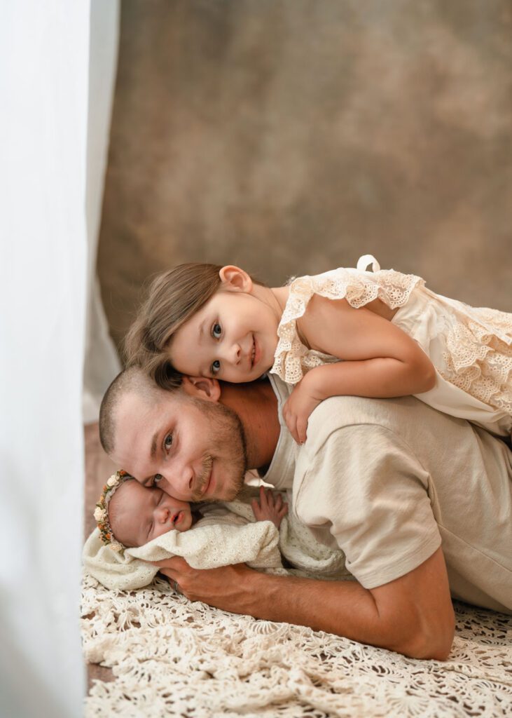 Dad cuddling his two daughters with big sister on his back during a newborn session near Roswell, Georgia.
