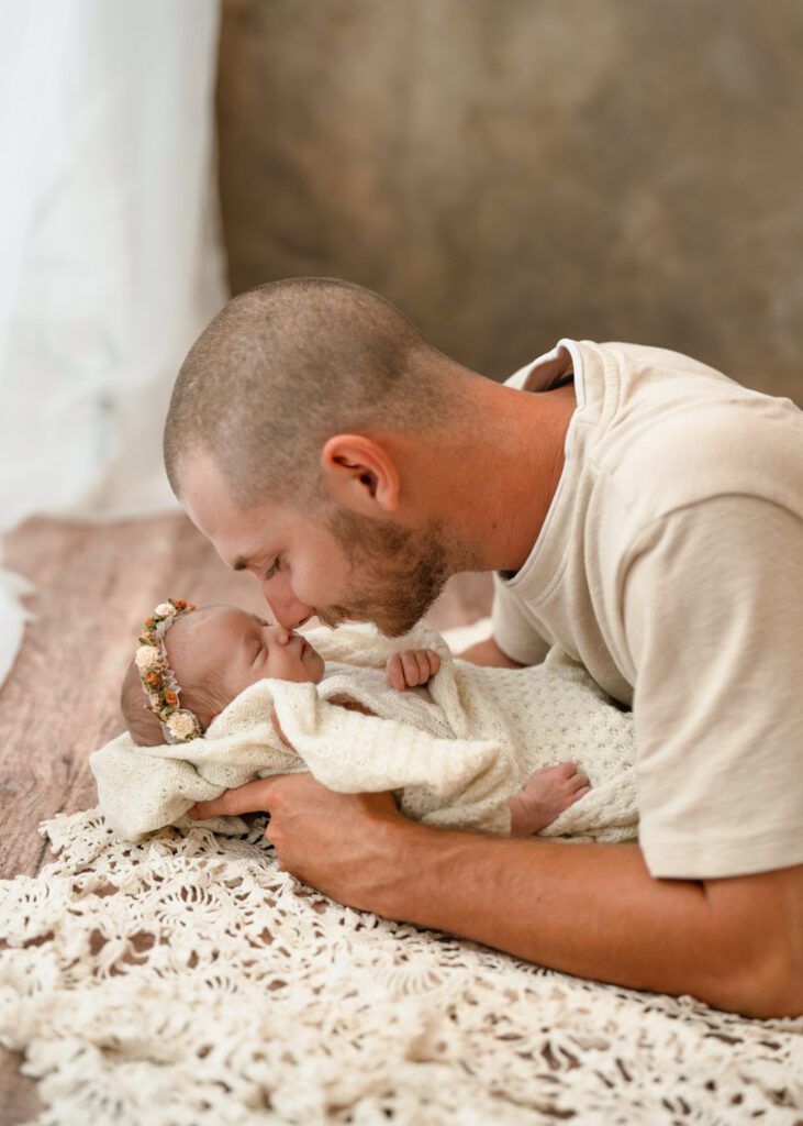 Dad holding his sleeping newborn daughter wrapped in crochet with a floral headband for a Roswell newborn photographer.