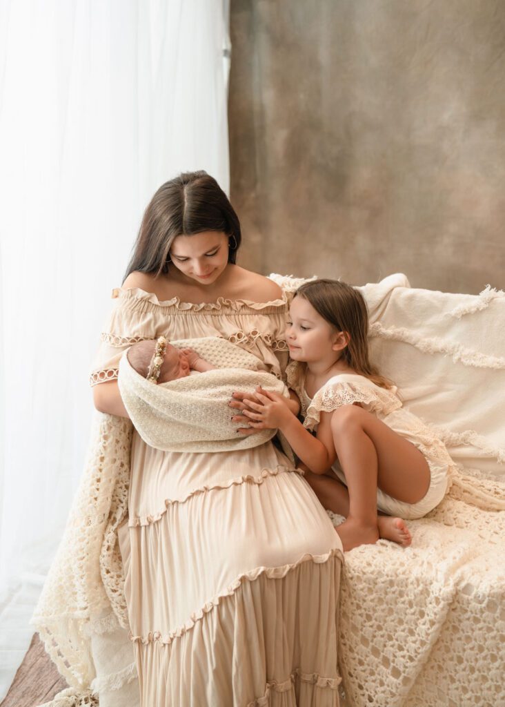Mom and daughter snuggling beside a bright window in matching beige outfits during Roswell newborn photos.