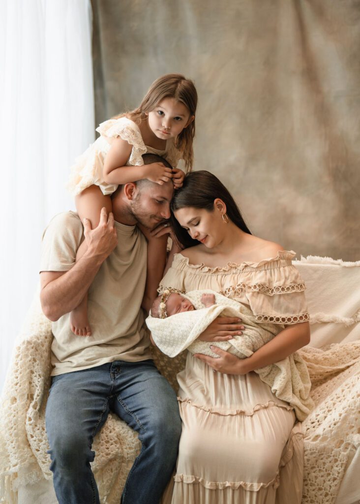 Daughter sitting on dad’s shoulders as mom cradles the newborn for a Roswell newborn photographer.