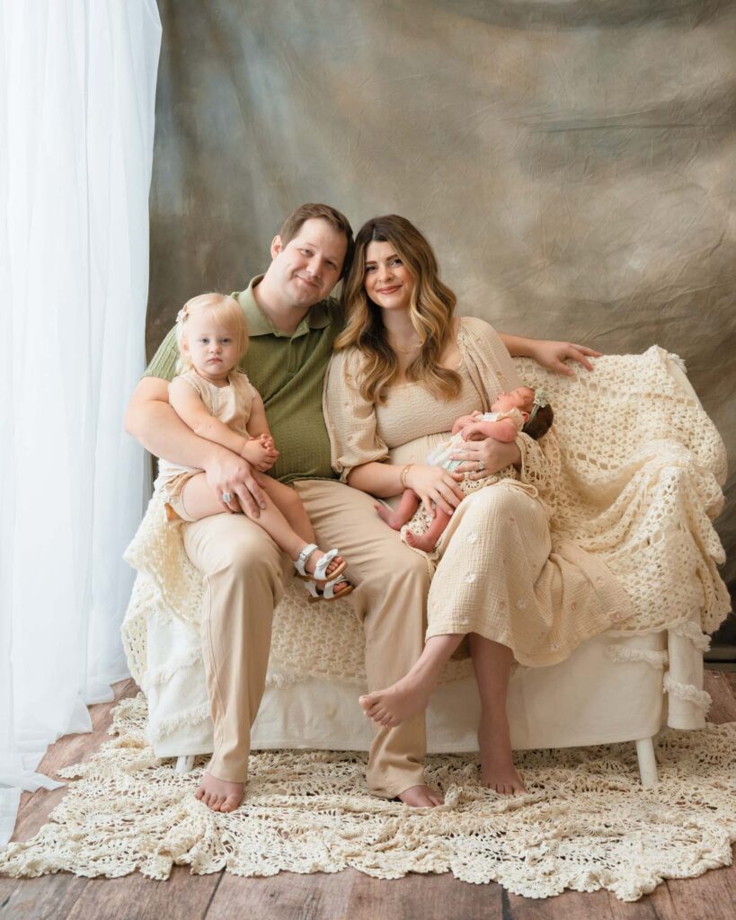 Parents sitting with their two daughters beside a bright window in coordinated cream and green outfits.