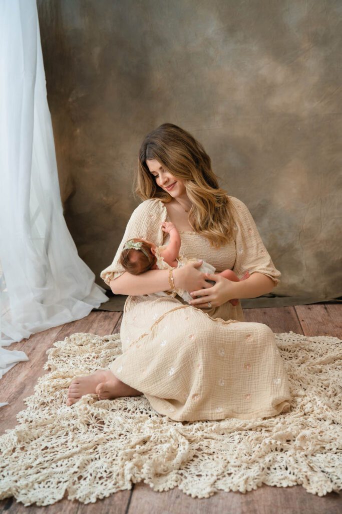 Mom in a beige smocked dress sitting on a blanket while holding her newborn daughter for Sandy Springs newborn photos.