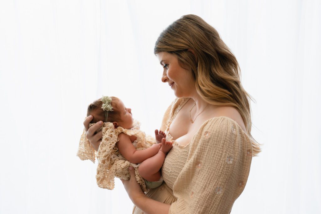 Mother in a cream dress looking down at her newborn daughter in a vintage lace outfit for Sandy Springs newborn photos.