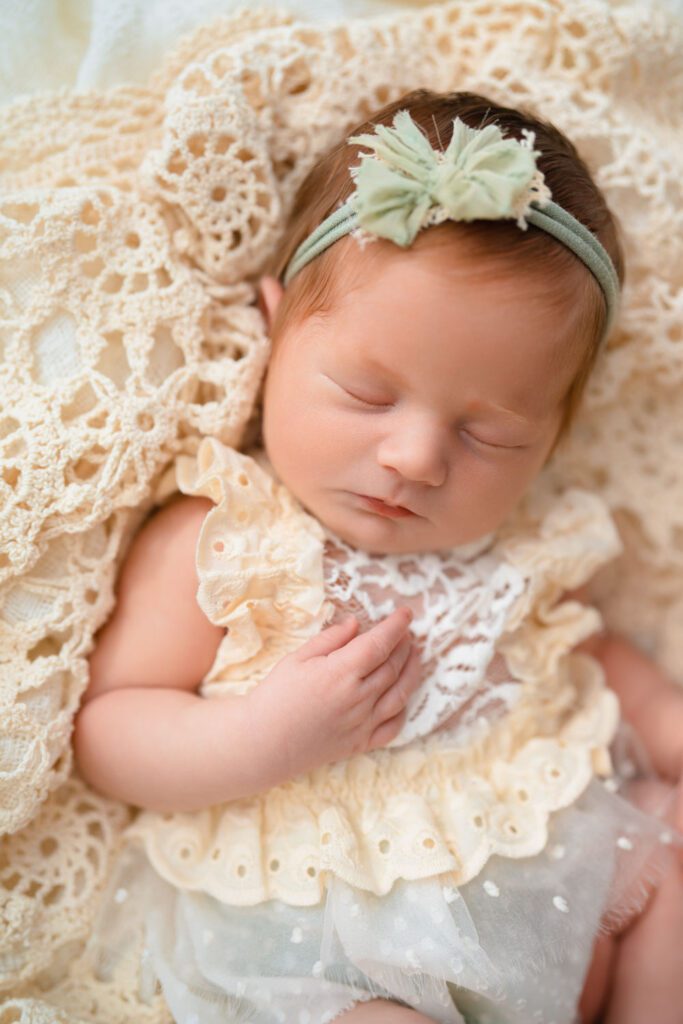 Red-haired newborn baby girl in a cream and sage romper sleeping on a crochet blanket.