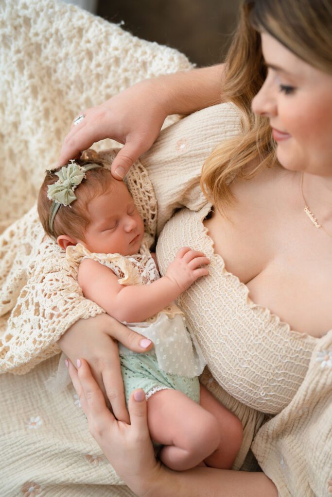 Mom holding her sleeping newborn daughter as dad reaches in to touch her head during a Sandy Springs newborn session.