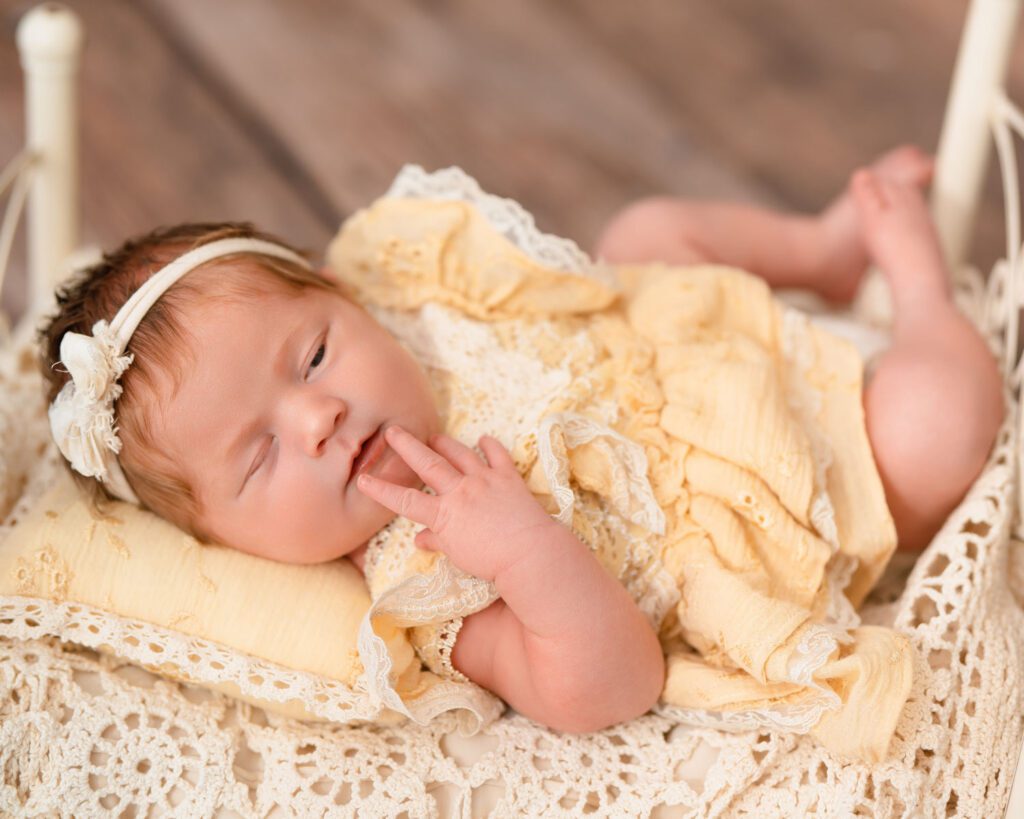 Newborn baby girl in a yellow lace outfit resting on a matching pillow and antique crochet blanket.
