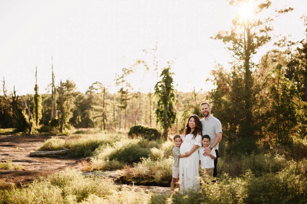 family of four standing closely looking at the camera in front of a forest.