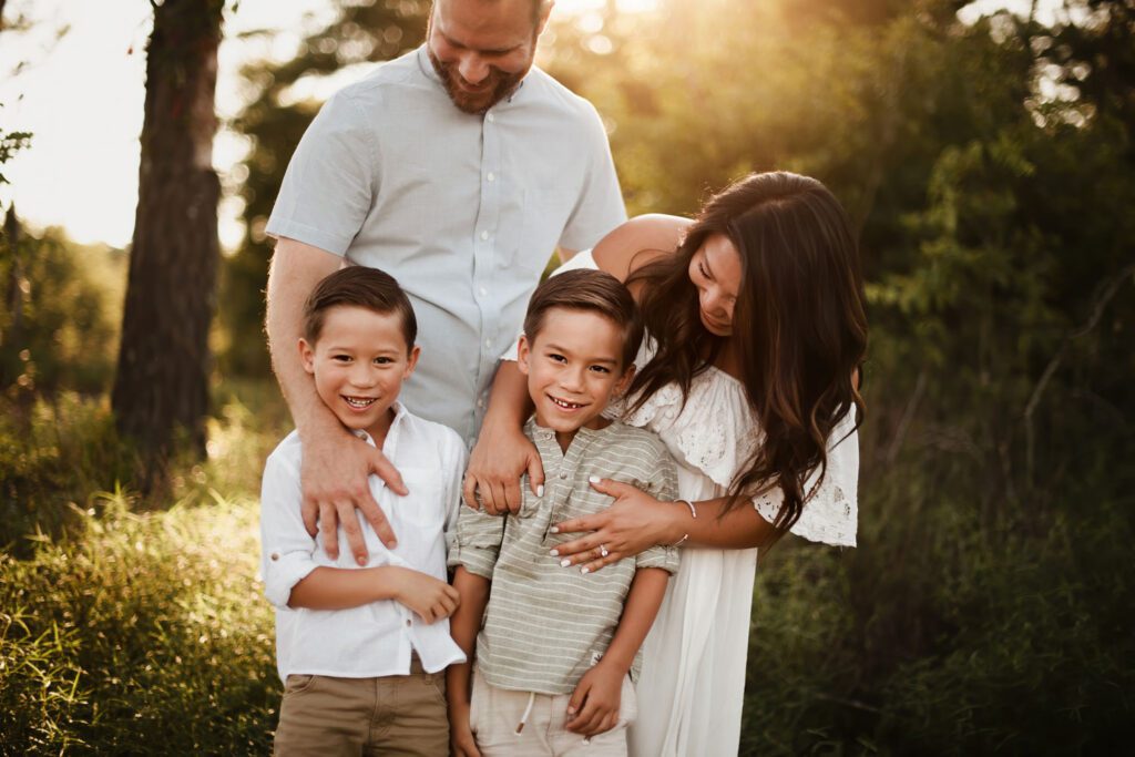 family of four standing close together and laughing outdoors at sunset.