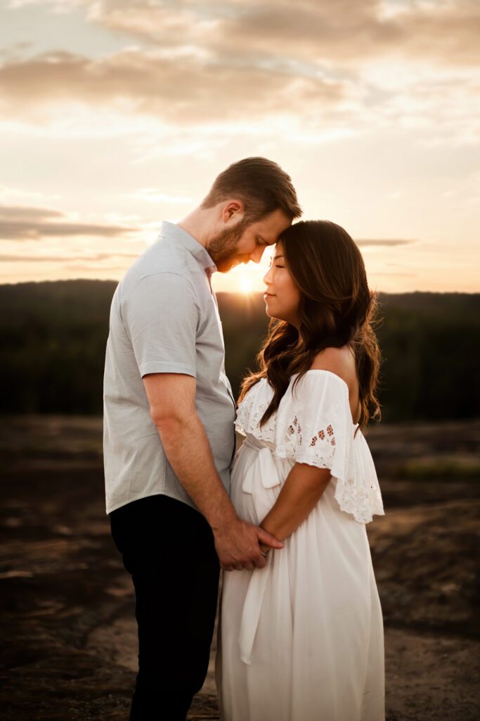 expecting couple standing closely holding hands outdoors with the Arabia Mountain crater pools in the background in Stonecrest, GA.