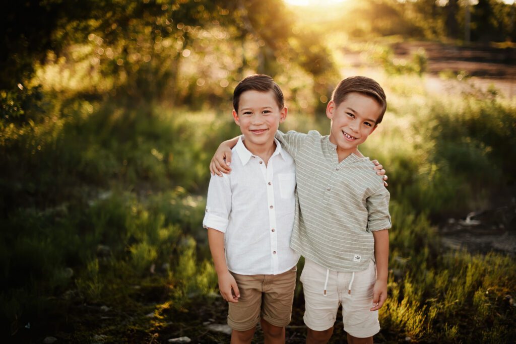 Two brothers standing together in warm golden light with softly blurred greenery in the background.