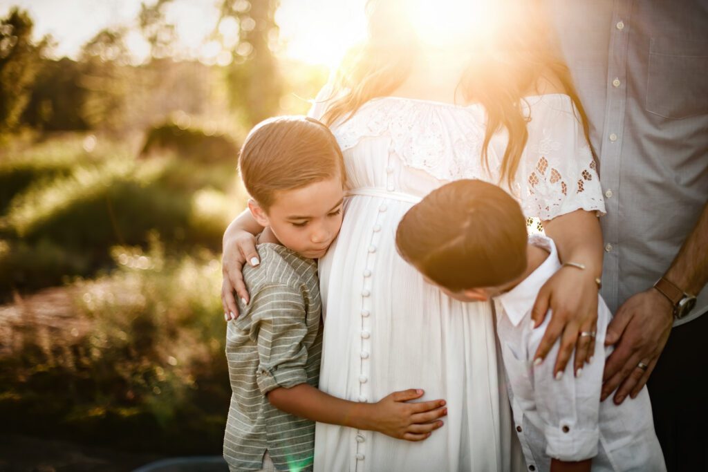 close up of twin brothers touching their mother's pregnant belly at golden hour outdoors.