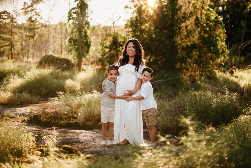 Pregnant woman in a white gown standing with two children in warm golden light during an Arabia Mountain maternity session.