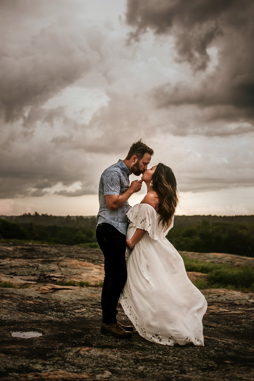Pregnant woman in a white gown kissing her husband on the Quarry Ruins at Arabia Mountain during a storm