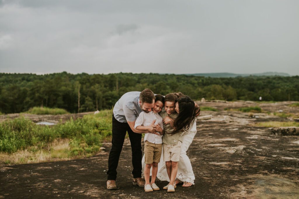 family of four bending down and hugging outdoors on rocky terrain at Arabia Mountain in Stonecrest.