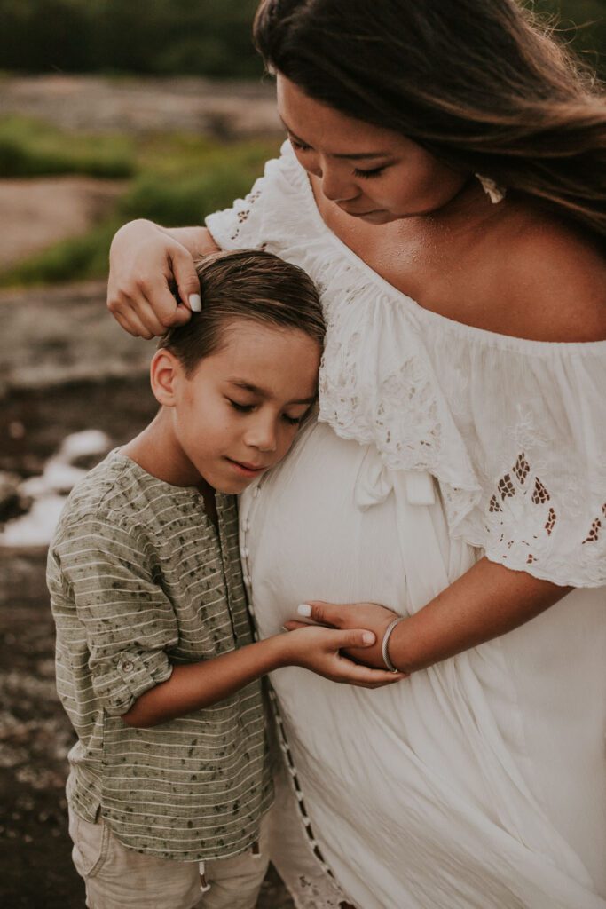 son resting his head peacefully on his mother's pregnant belly as she gently touches his hair.