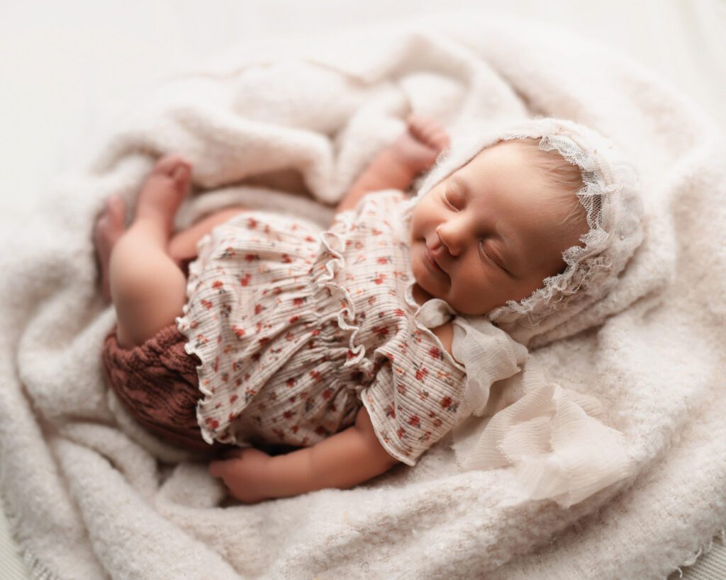 three week Newborn baby girl wearing a pink floral shirt and bloomers with antique bonnet