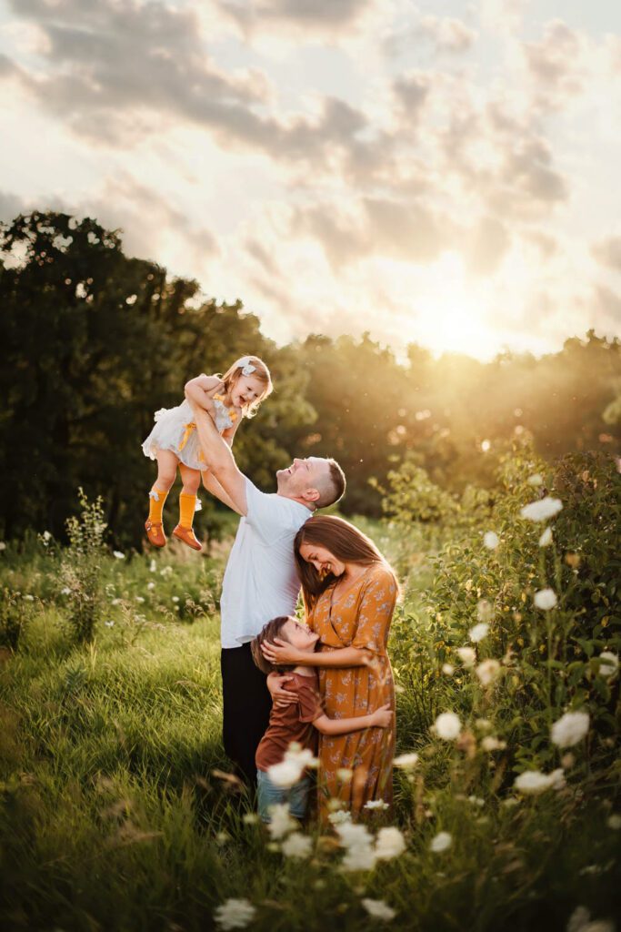 Mom in a mustard dress hugging her son in a rust colored shirt while dad in a white shirt holds his daughter in yellow socks.